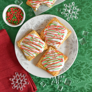 Festive homemade strawberry hand pies topped with white icing and red and green drizzle, served on a snowflake-patterned plate with Christmas sprinkles.